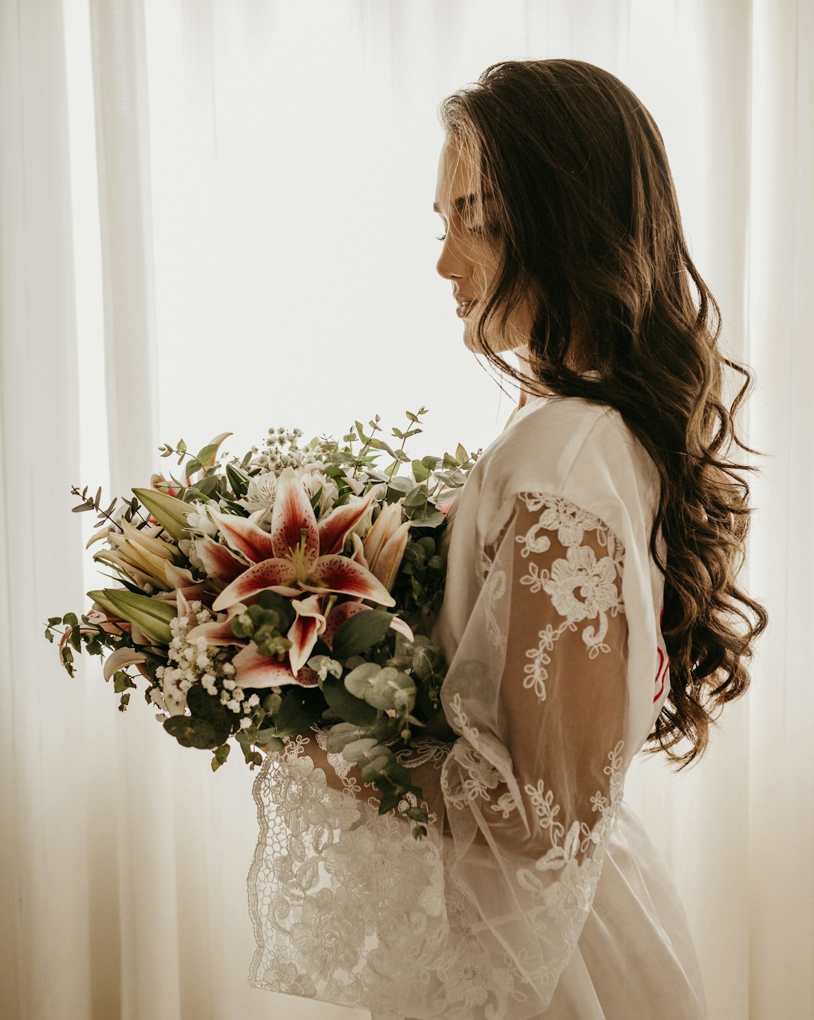 A bride in soft window light holding her bouquet