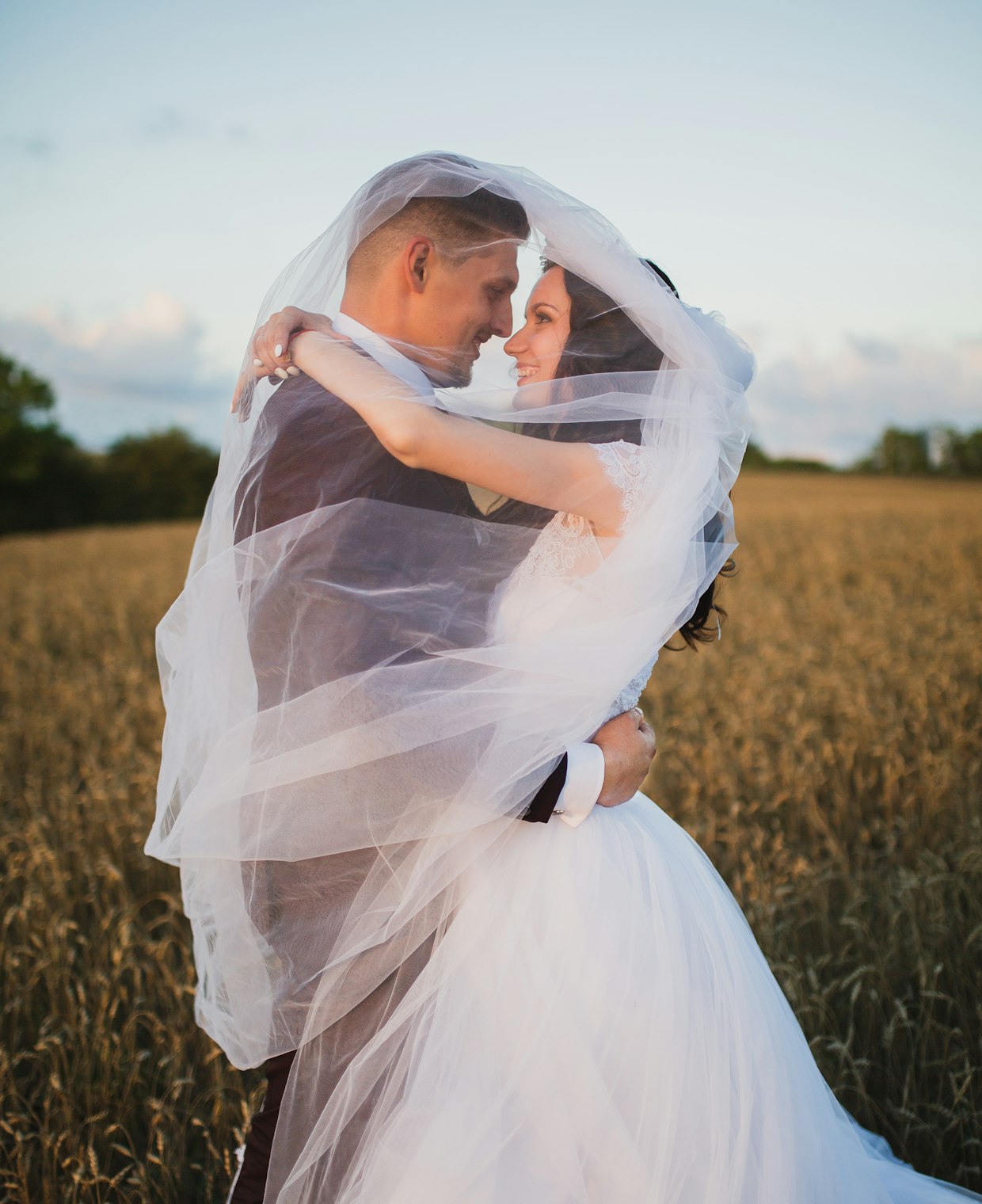 A newly married couple wrapped together beneath a soft veil